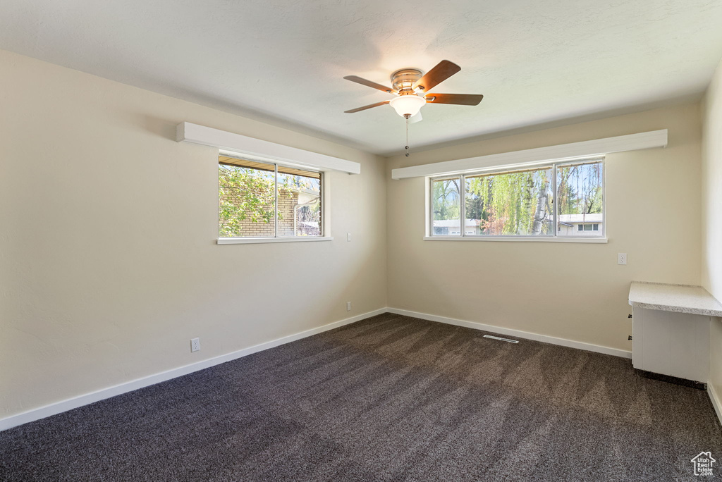 Unfurnished room featuring baseboards, ceiling fan, visible vents, and dark carpet