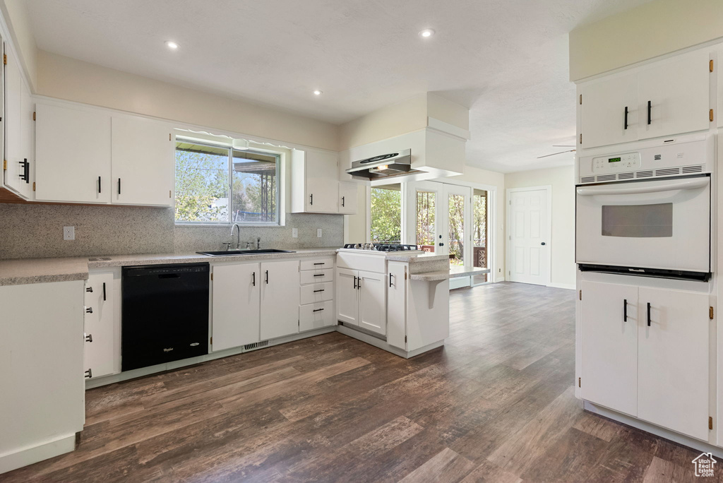 Kitchen with white oven, a sink, dark wood-style floors, black dishwasher, and extractor fan