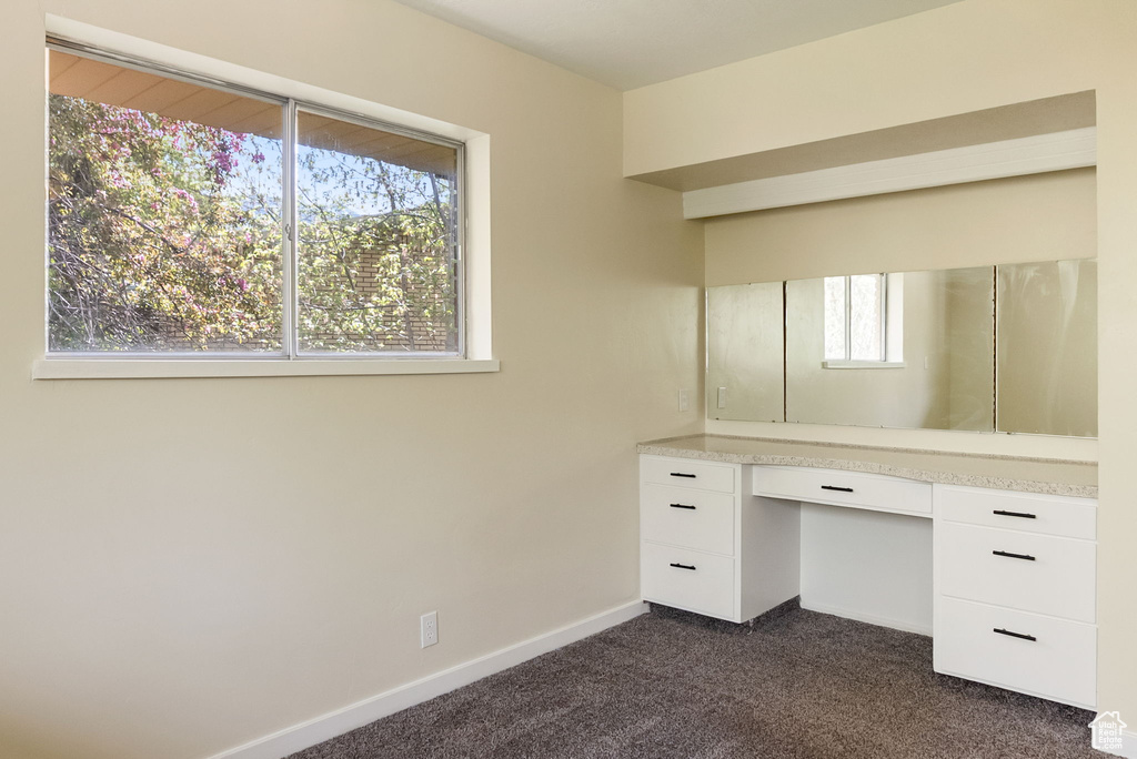 Unfurnished office featuring baseboards, built in study area, and dark colored carpet