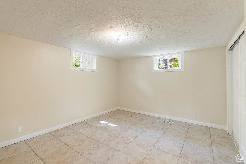 Basement featuring light tile patterned flooring, a textured ceiling, plenty of natural light, and baseboards