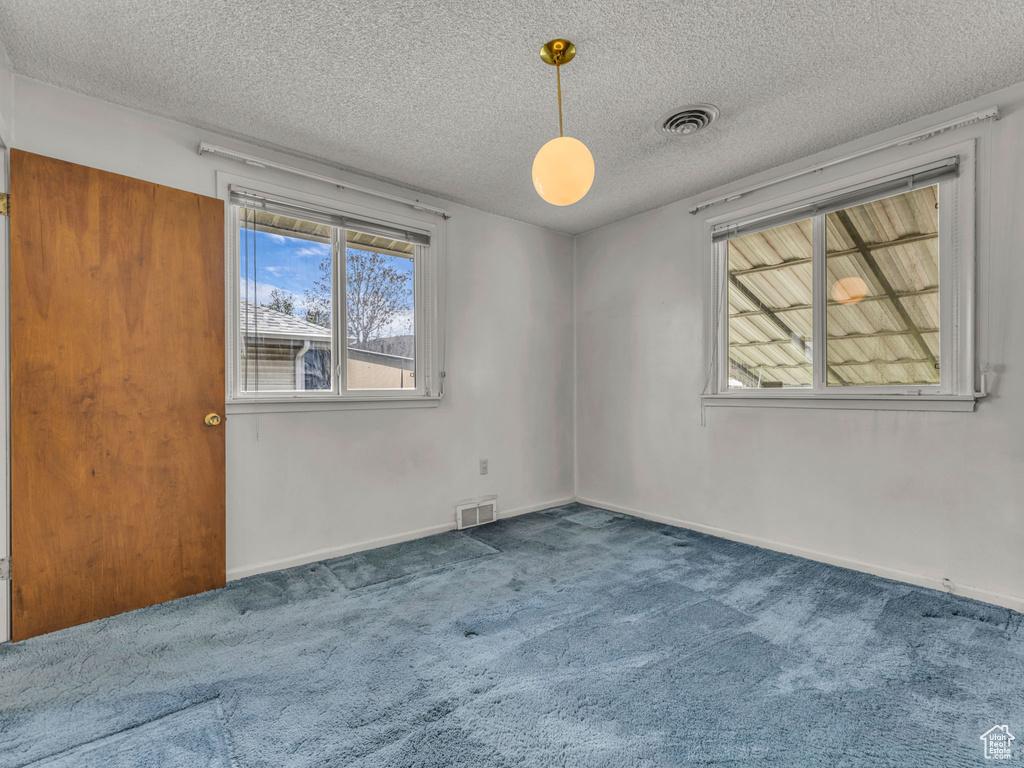 Empty room with carpet flooring, a textured ceiling, and visible vents