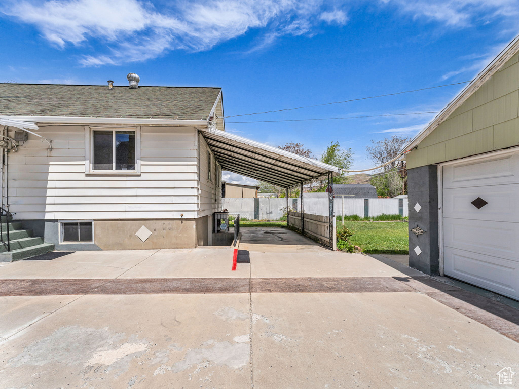 View of property exterior with fence, a carport, driveway, and roof with shingles