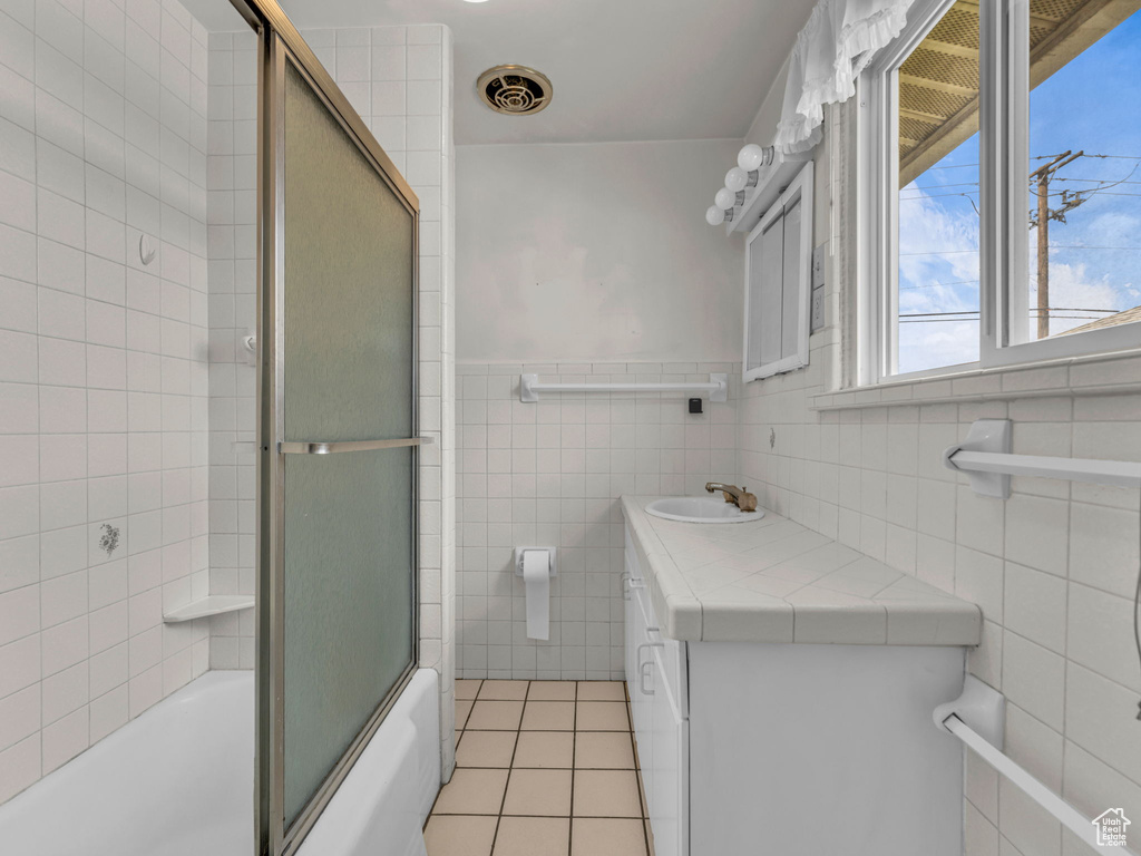Bathroom with tile walls, vanity, a wainscoted wall, tile patterned floors, and combined bath / shower with glass door