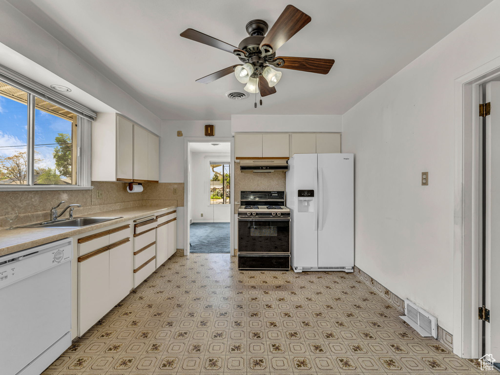 Kitchen featuring a sink, white appliances, tasteful backsplash, under cabinet range hood, and visible vents