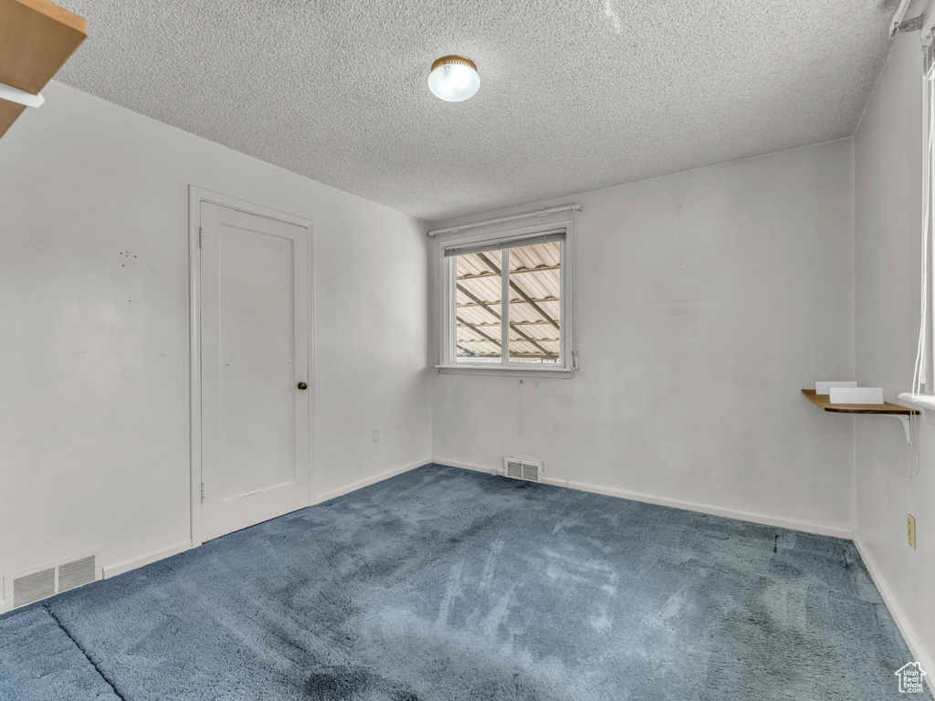 Unfurnished room with a textured ceiling, visible vents, and dark carpet