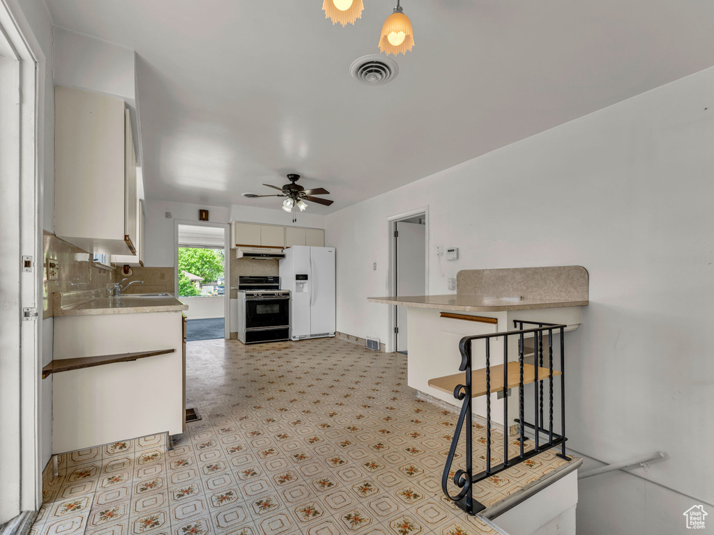 Kitchen with white refrigerator with ice dispenser, light countertops, under cabinet range hood, a sink, and gas stove