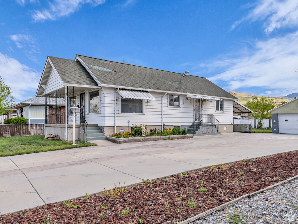 Ranch-style home featuring a porch, driveway, a garage, fence, and a shingled roof