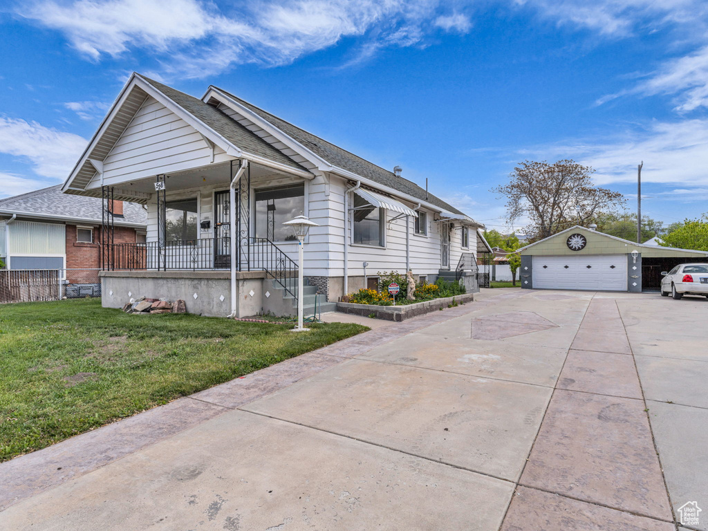 View of front of home featuring a front lawn, covered porch, a shingled roof, concrete driveway, and an outbuilding