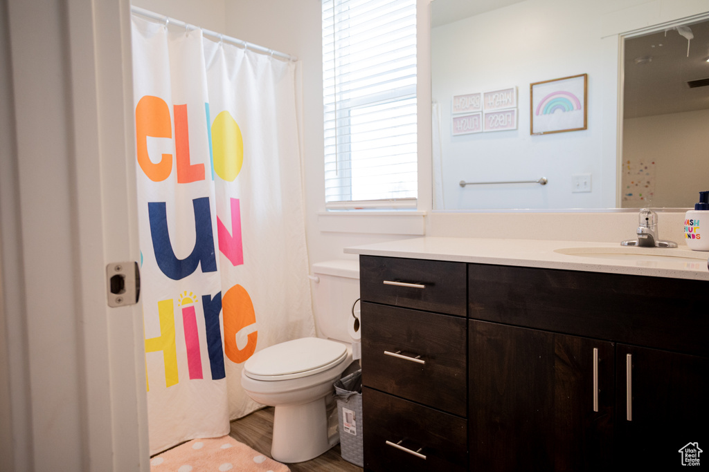 Full bath with vanity, toilet, a shower with shower curtain, wood finished floors, and visible vents