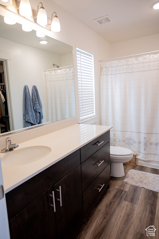 Bathroom featuring a shower with curtain, visible vents, wood finished floors, vanity, and toilet