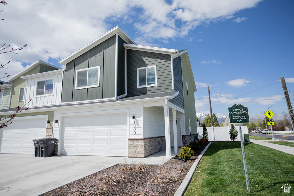 View of property exterior featuring board and batten siding, a lawn, a garage, concrete driveway, and stone siding