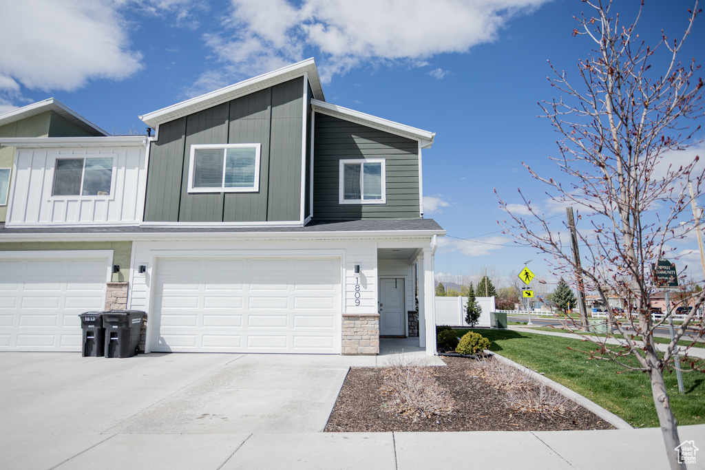 View of front of home featuring fence, stone siding, a garage, board and batten siding, and concrete driveway