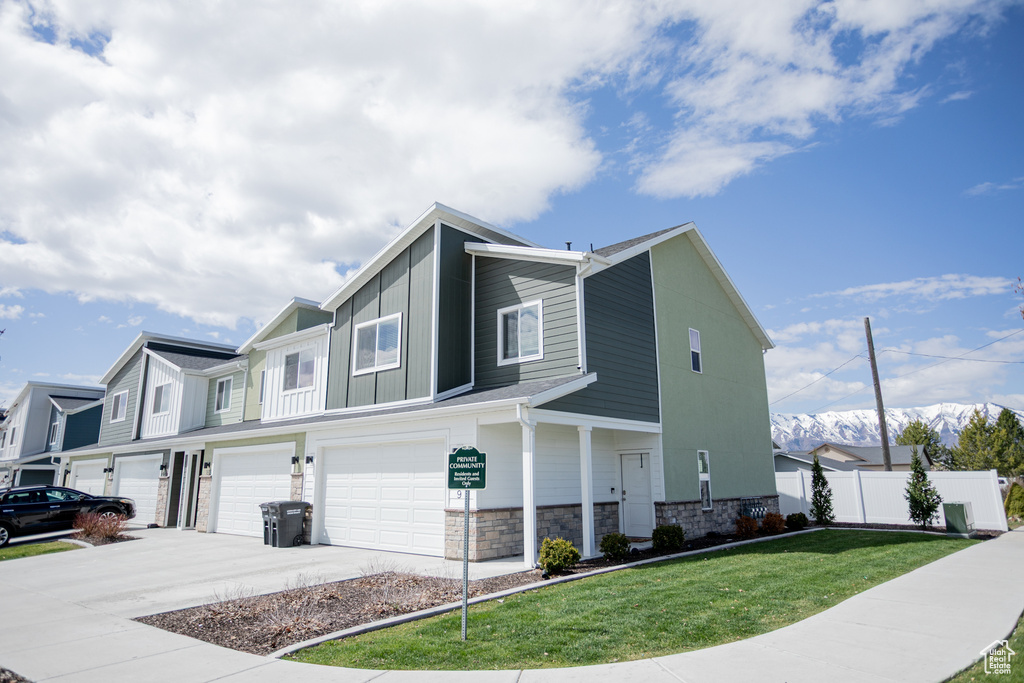 View of front facade featuring a garage, fence, a front yard, stone siding, and driveway