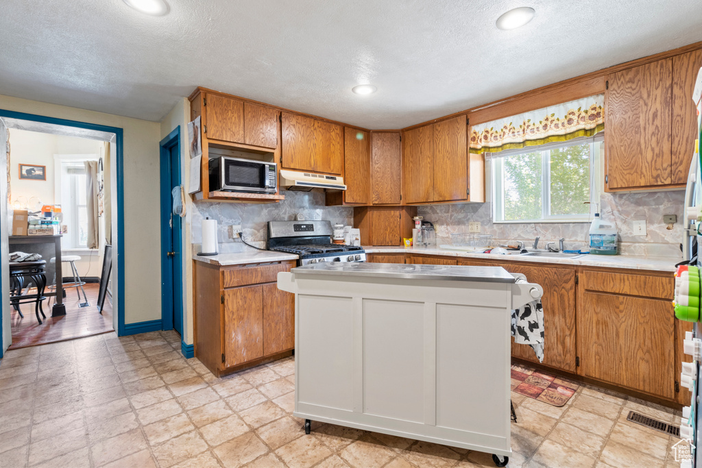 Kitchen with stainless steel appliances, under cabinet range hood, light countertops, backsplash, and a textured ceiling