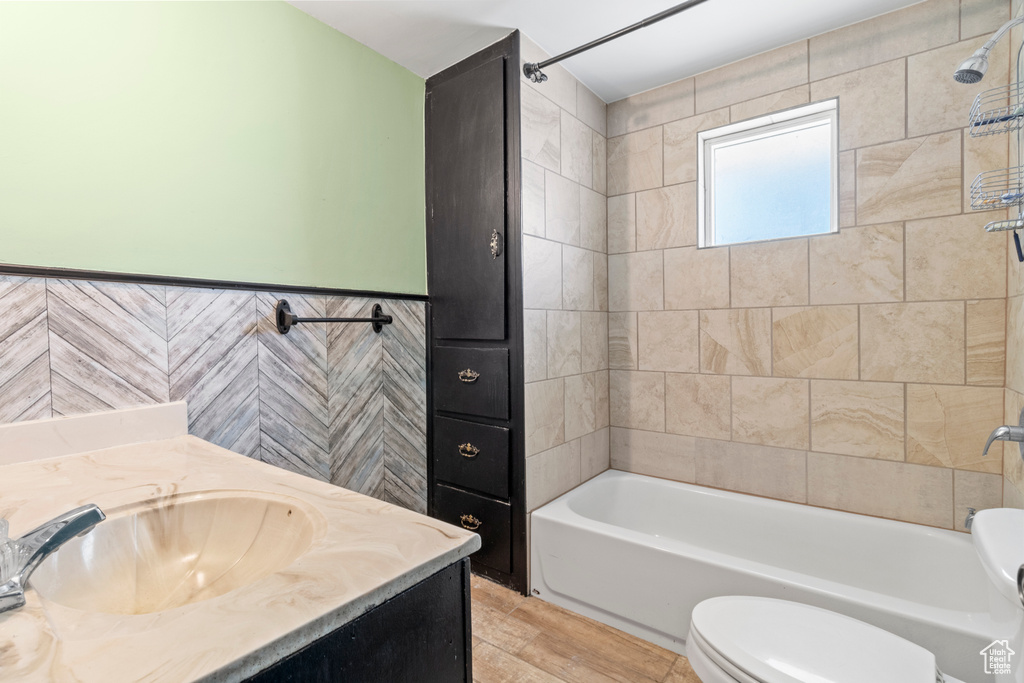 Full bath featuring toilet, vanity, shower / washtub combination, tile walls, and wainscoting