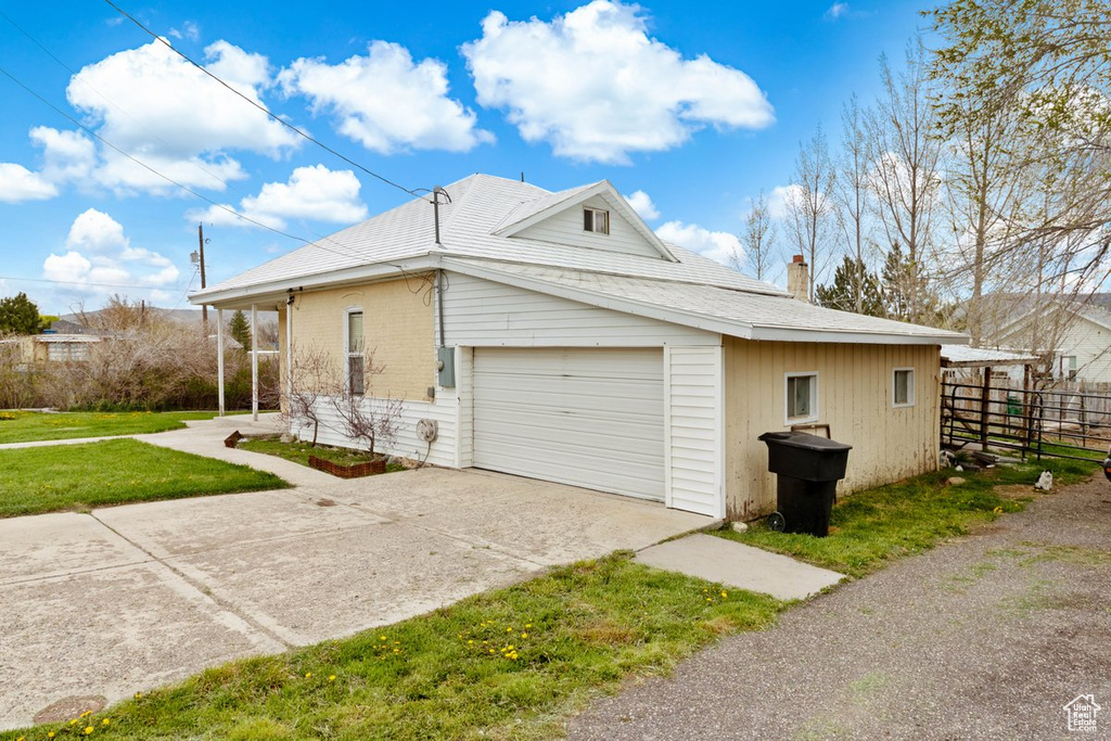 View of side of home with driveway, a chimney, a garage, fence, and a yard