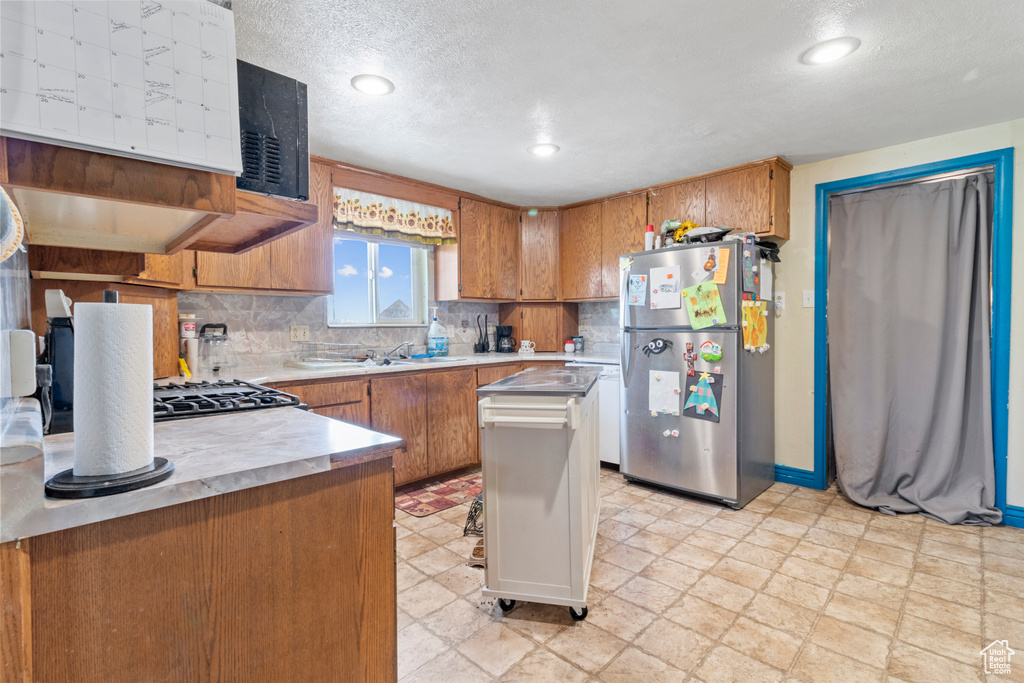 Kitchen featuring freestanding refrigerator, brown cabinetry, light countertops, backsplash, and recessed lighting