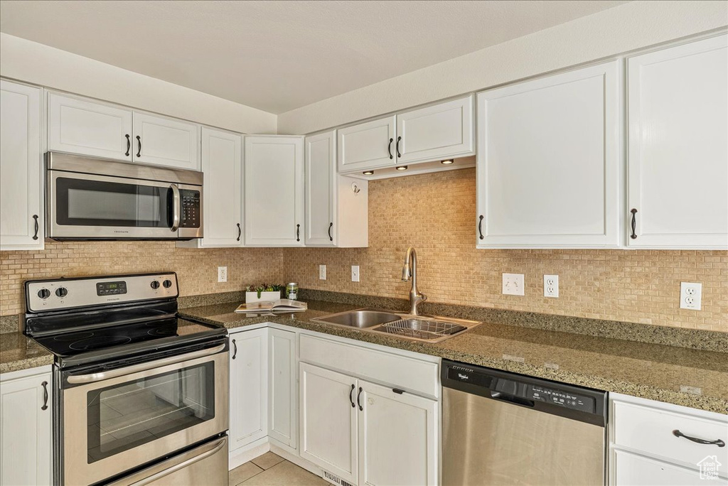 Kitchen featuring a sink, appliances with stainless steel finishes, decorative backsplash, and white cabinetry
