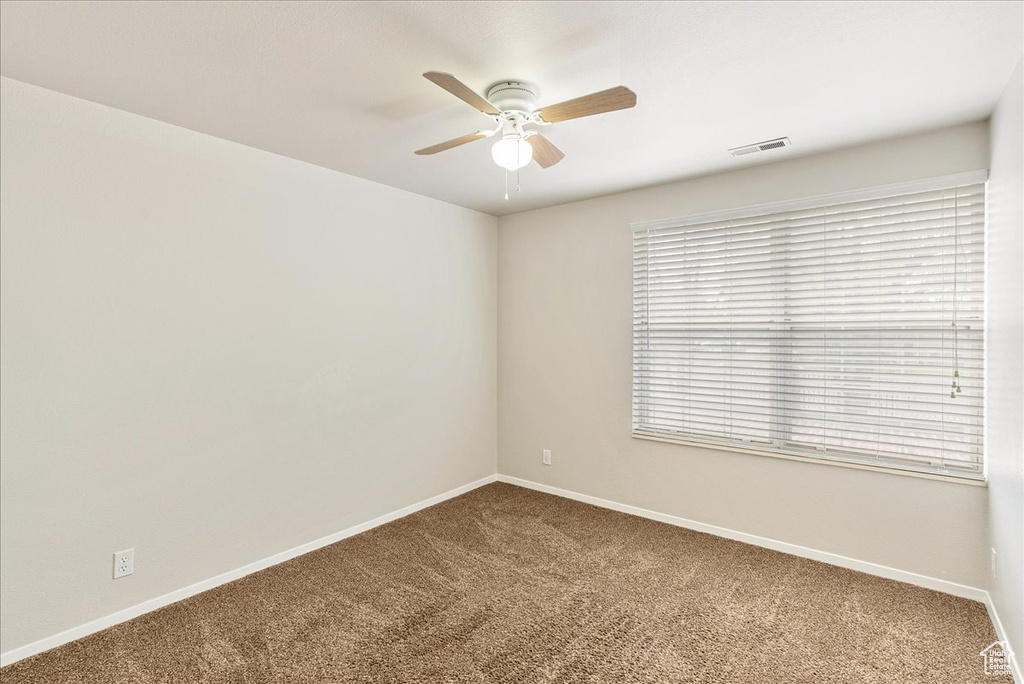 Empty room featuring visible vents, carpet, ceiling fan, and baseboards