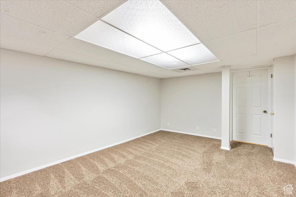 Finished below grade area featuring carpet flooring, baseboards, visible vents, and a drop ceiling