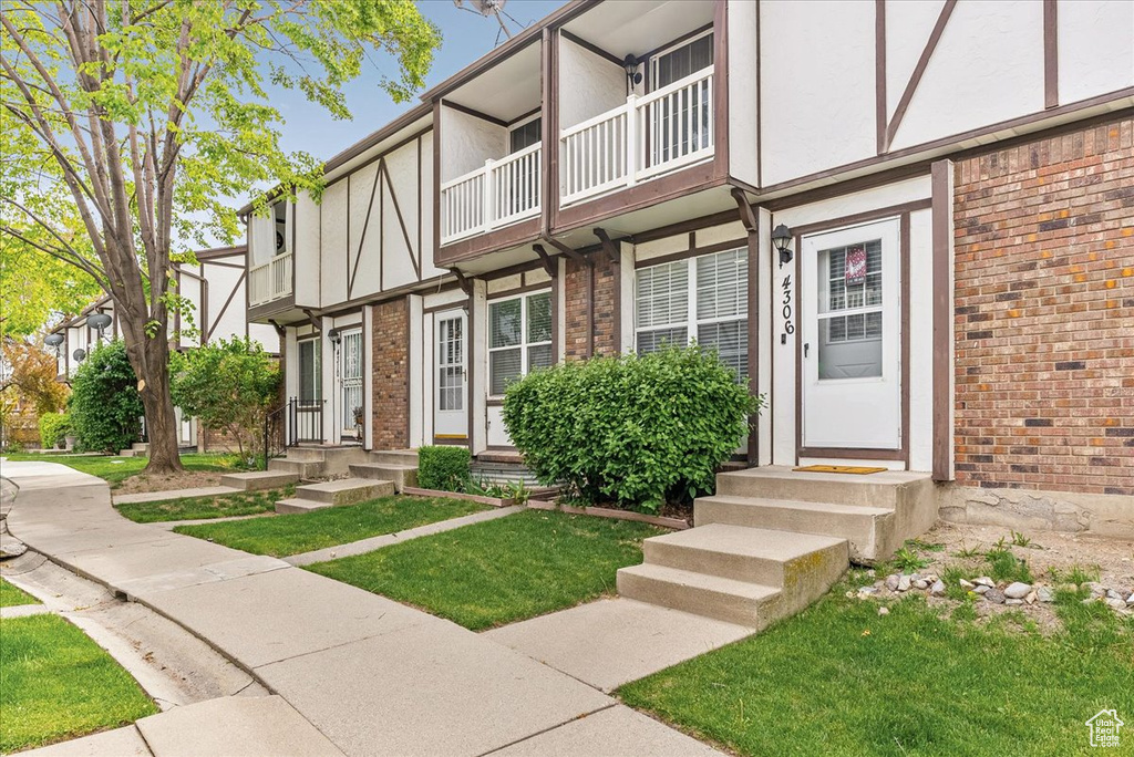 Entrance to property with brick siding, a yard, stucco siding, and a balcony