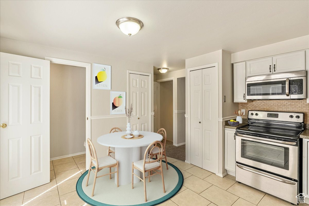 Kitchen featuring white cabinets, light countertops, stainless steel appliances, light tile patterned floors, and backsplash