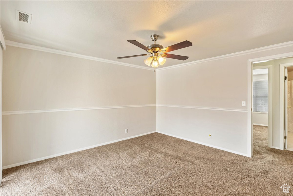 Carpeted empty room with crown molding, baseboards, a ceiling fan, and visible vents