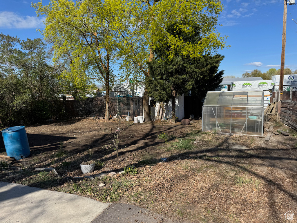 View of yard featuring fence, a greenhouse, and an outbuilding