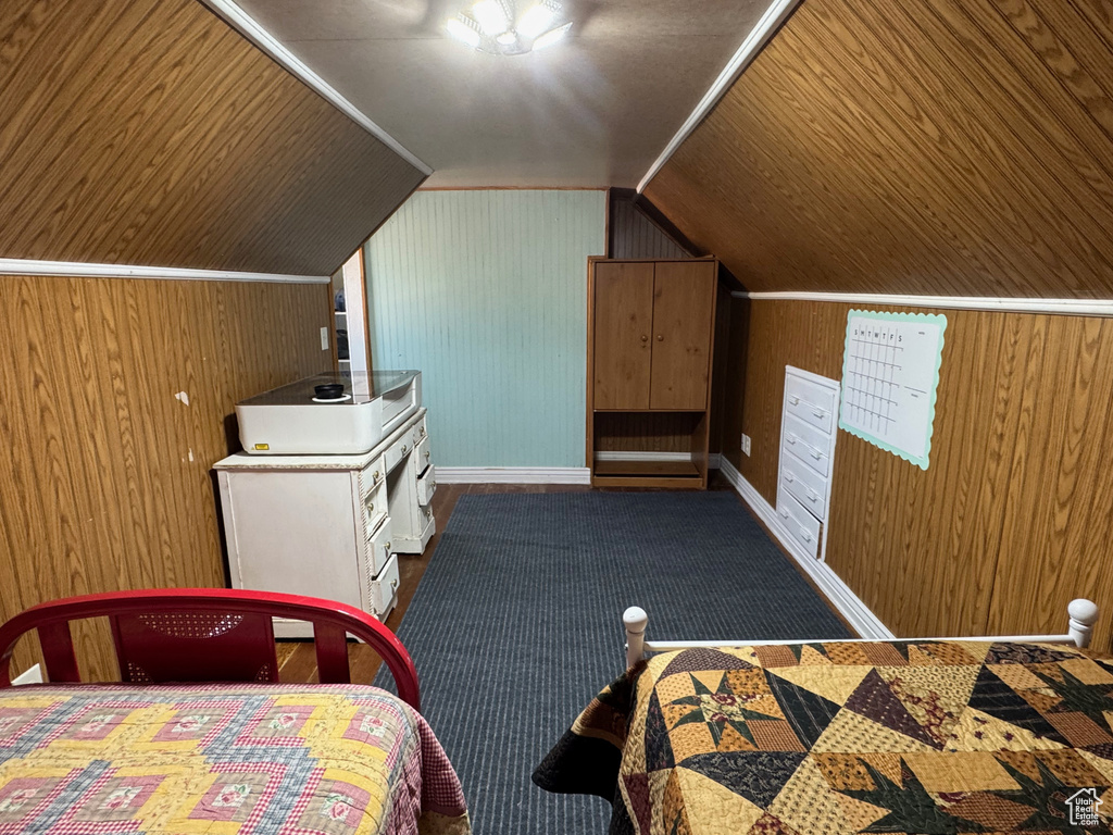 Carpeted bedroom featuring baseboards, wooden walls, and vaulted ceiling