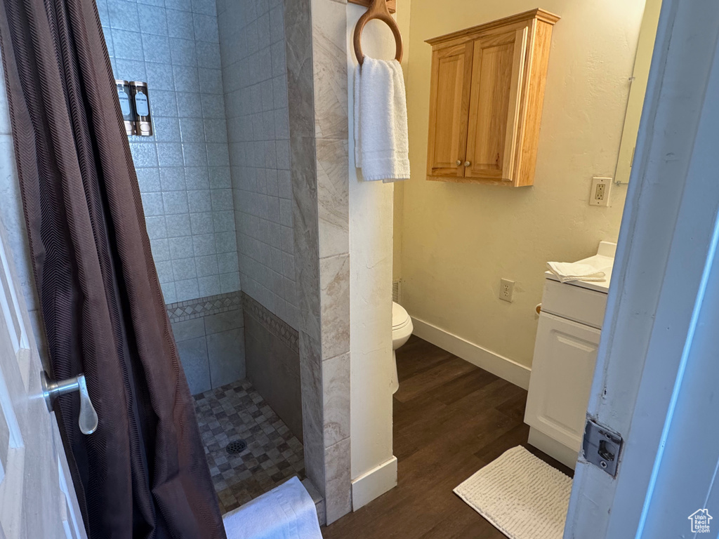 Full bath with vanity, wood finished floors, toilet, baseboards, and tiled shower