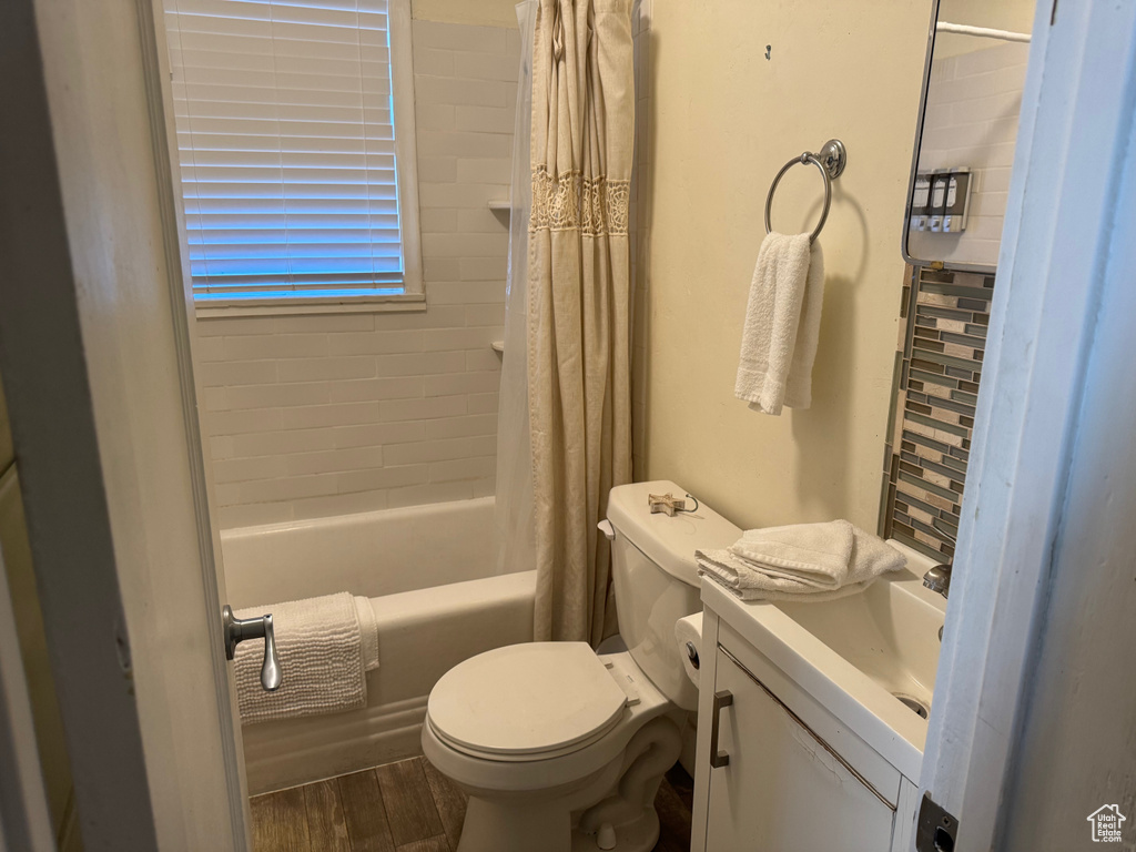 Bathroom featuring vanity, shower / bathtub combination with curtain, wood finished floors, and toilet
