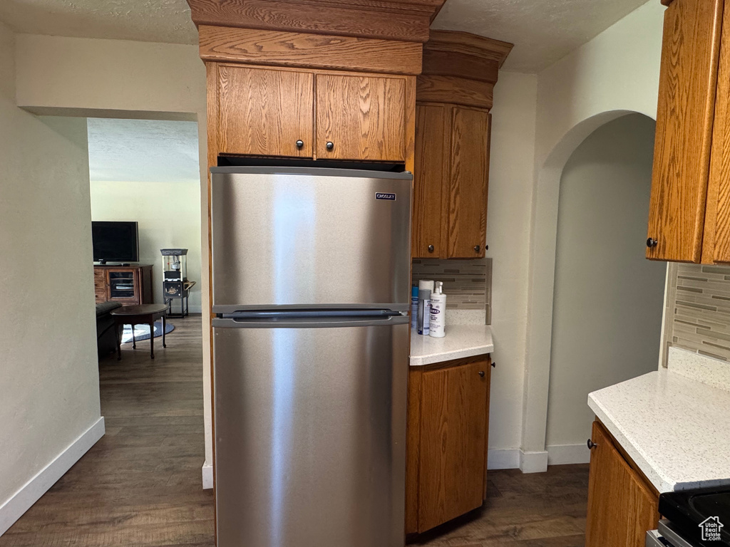 Kitchen featuring tasteful backsplash, brown cabinets, baseboards, freestanding refrigerator, and dark wood-type flooring