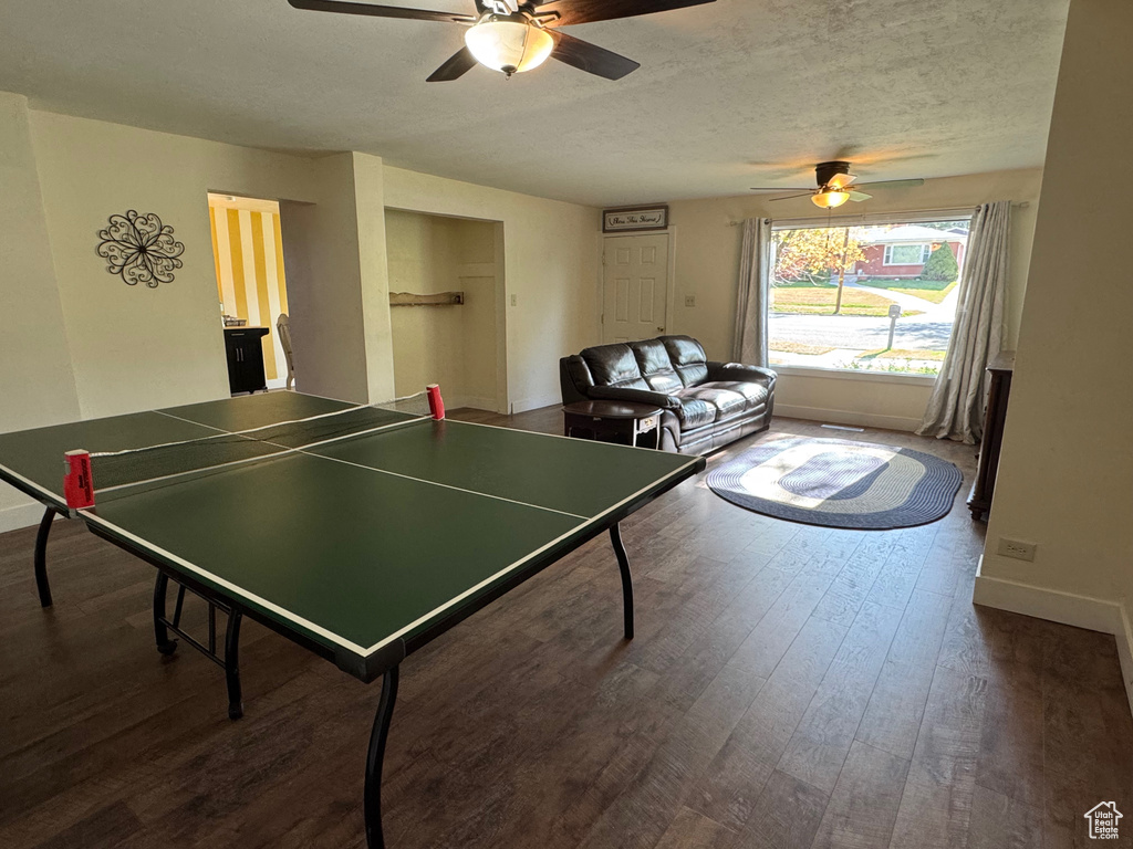 Recreation room featuring a textured ceiling, ceiling fan, baseboards, and dark wood-type flooring