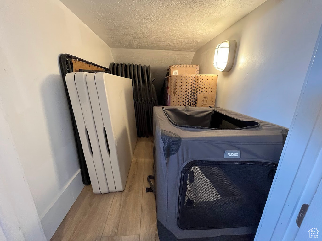 Clothes washing area with light wood-type flooring, a textured ceiling, radiator heating unit, and radiator