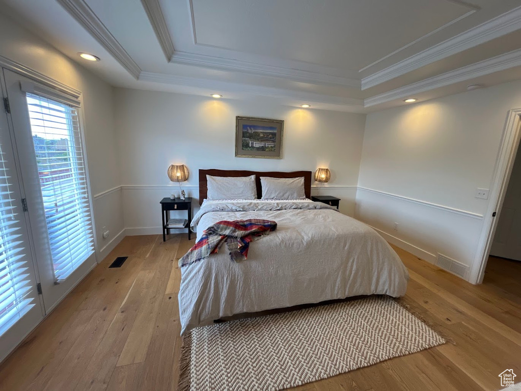 Bedroom with visible vents, ornamental molding, a raised ceiling, and light wood-style floors