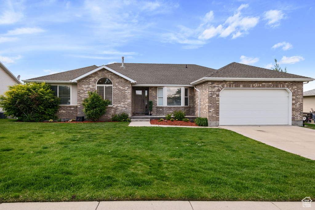Ranch-style home with an attached garage, driveway, a front yard, and brick siding