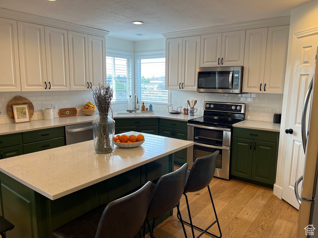 Kitchen with a sink, green cabinetry, stainless steel appliances, and white cabinets
