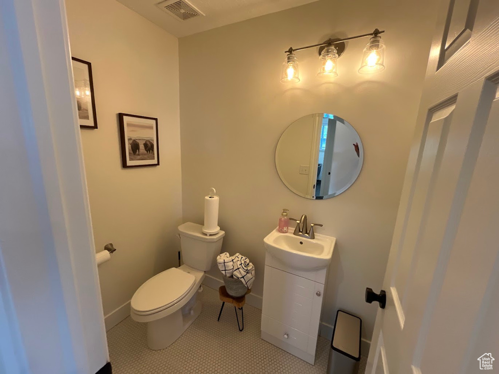 Half bath featuring visible vents, vanity, toilet, baseboards, and tile patterned floors