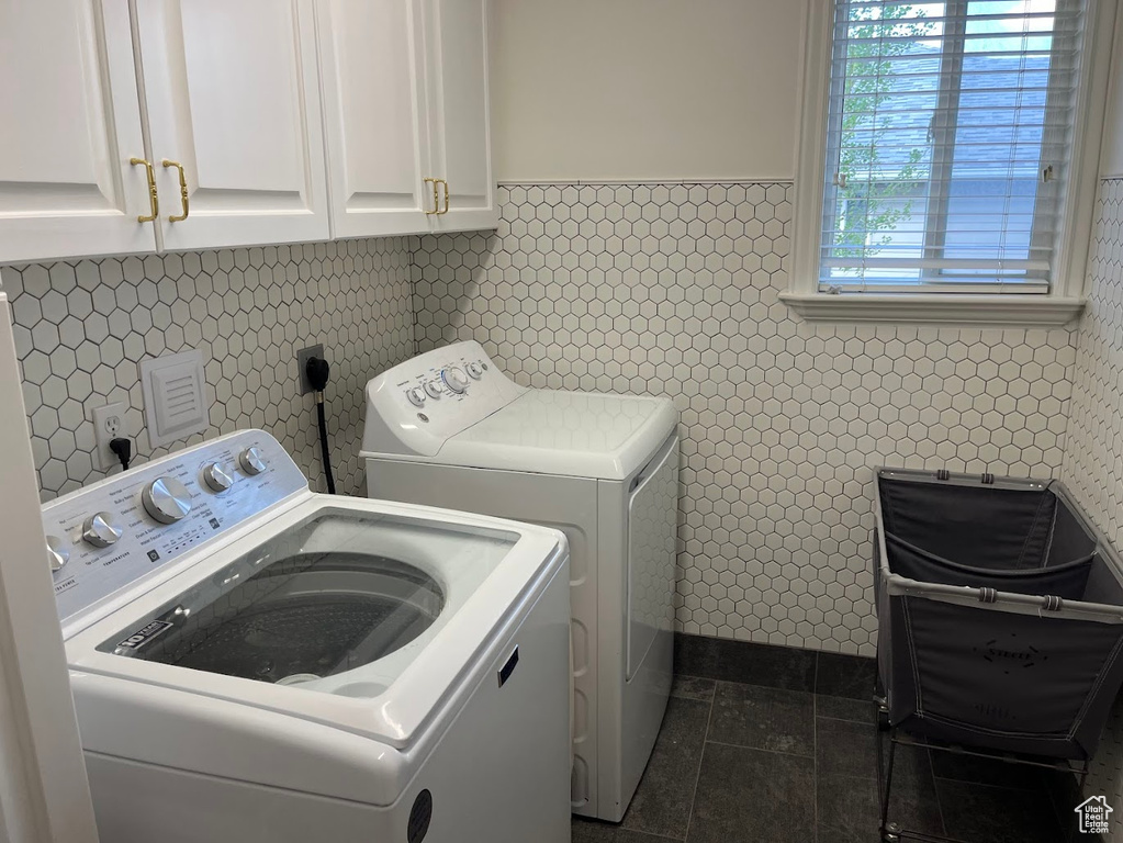 Laundry room featuring dark tile patterned flooring, a wainscoted wall, cabinet space, and washing machine and clothes dryer