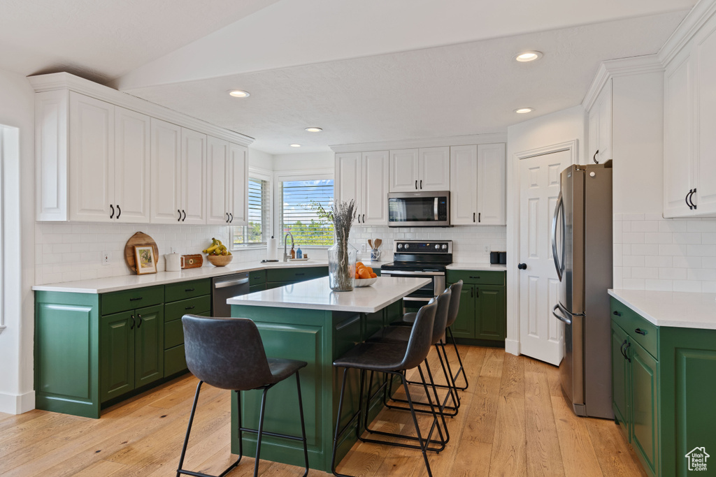 Kitchen featuring appliances with stainless steel finishes, green cabinetry, white cabinets, recessed lighting, and lofted ceiling
