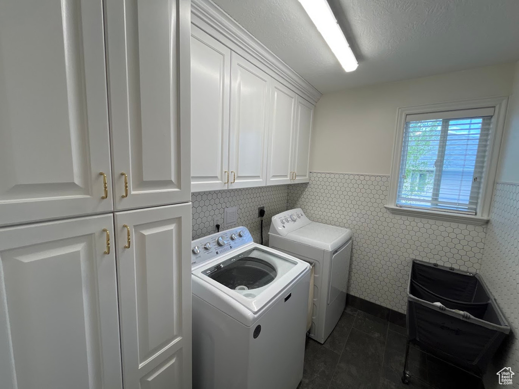 Laundry room with cabinet space, independent washer and dryer, a wainscoted wall, tile walls, and dark tile patterned flooring