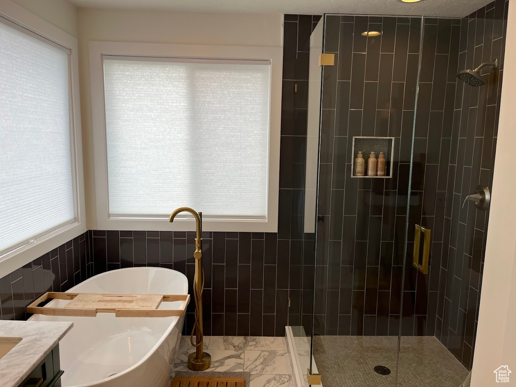 Bathroom with a freestanding tub, a shower stall, a wealth of natural light, and tile walls