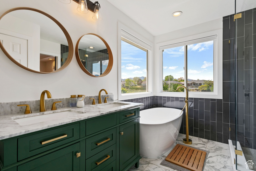 Full bathroom featuring marble look tiles, tile walls, recessed lighting, a freestanding tub, and double vanity