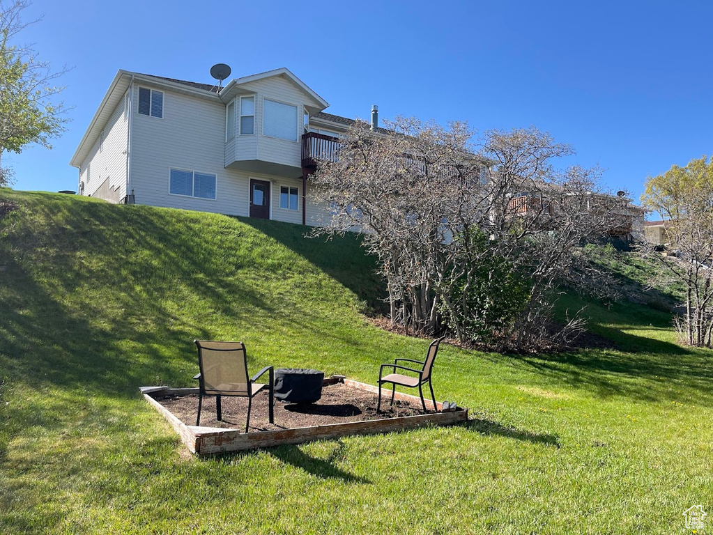 Rear view of property featuring a lawn, an outdoor fire pit, and a balcony