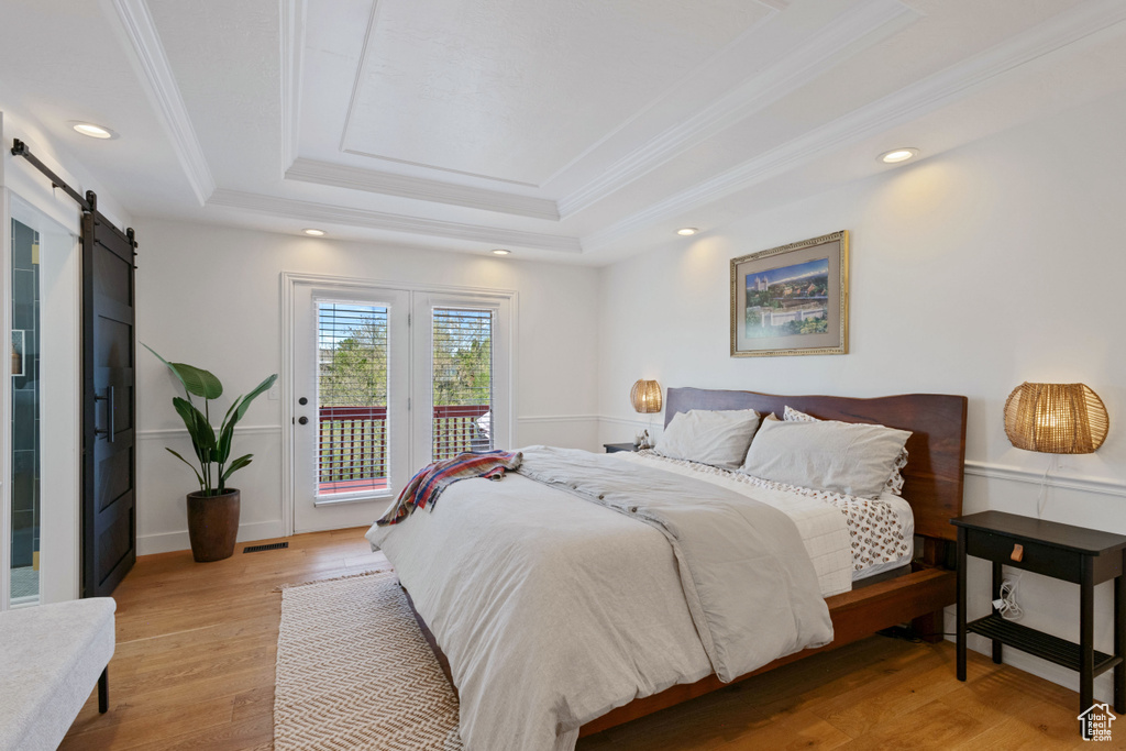 Bedroom featuring a tray ceiling, a barn door, access to outside, crown molding, and light wood-style floors
