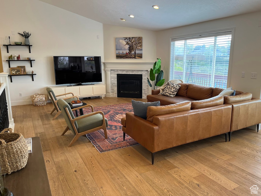 Living room featuring a fireplace, recessed lighting, baseboards, lofted ceiling, and light wood-type flooring