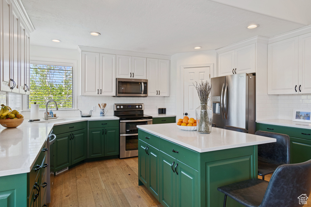 Kitchen featuring appliances with stainless steel finishes, green cabinetry, a sink, white cabinetry, and recessed lighting