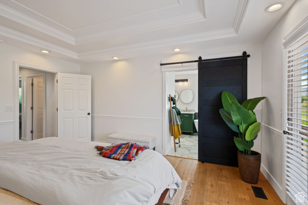 Bedroom featuring a raised ceiling, ornamental molding, light wood finished floors, a barn door, and recessed lighting