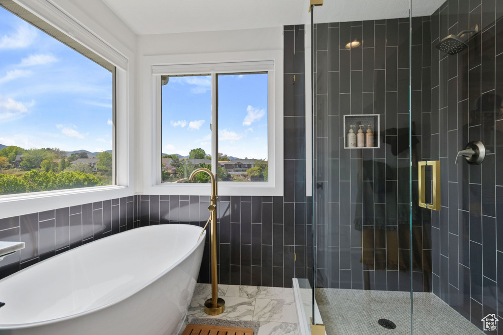 Full bath featuring marble finish flooring, tile walls, a shower stall, and a soaking tub