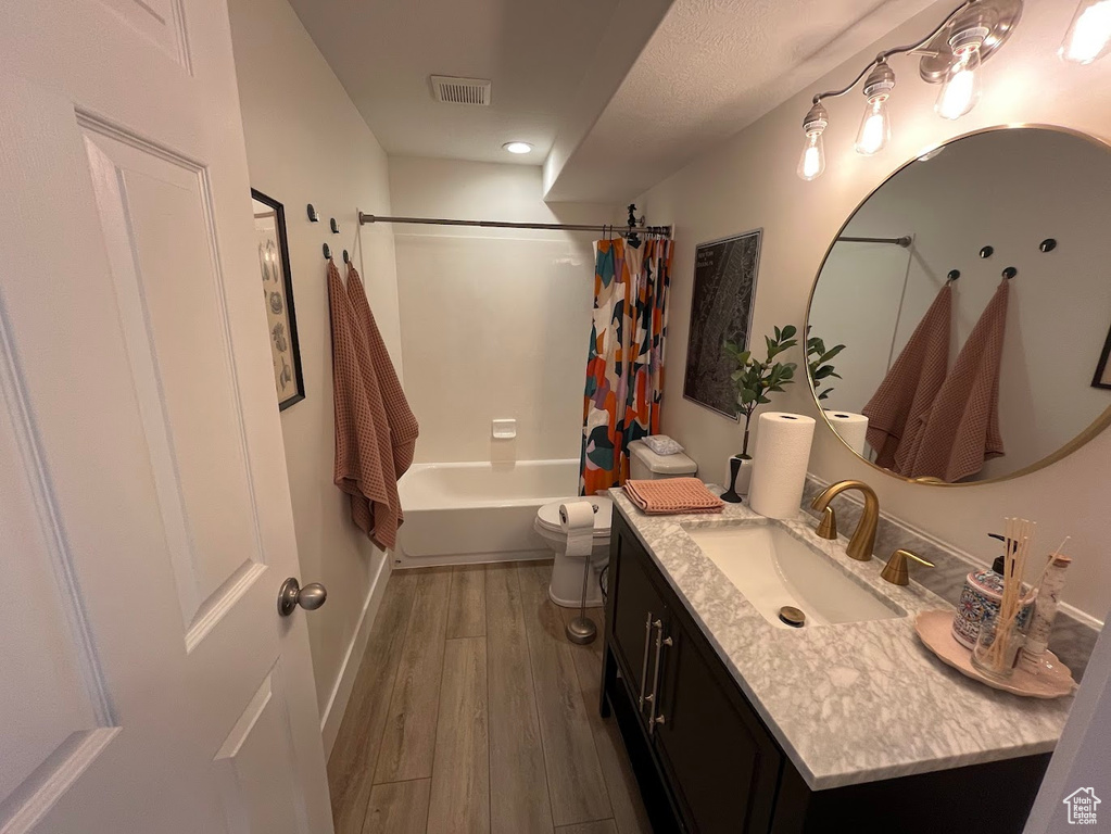 Full bathroom featuring shower / bath combination with curtain, visible vents, wood finished floors, vanity, and toilet